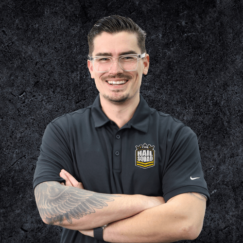 A person wearing glasses and a black polo shirt with a "Hail Squad" logo stands in front of a dark, textured backdrop reminiscent of their home environment, arms crossed and smiling.