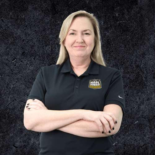 A person with long blonde hair in a black polo shirt stands with crossed arms, exuding a sense of confidence against the dark textured background—a home for their contemplative gaze.