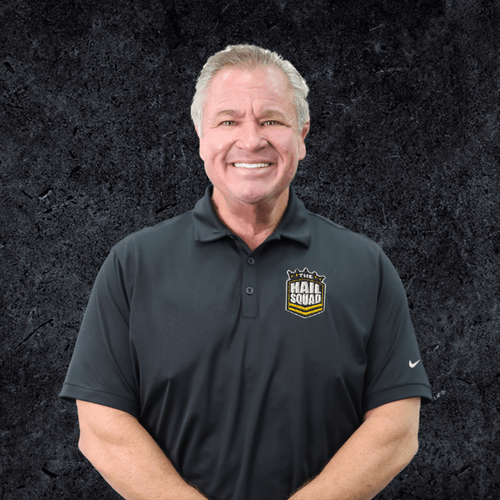 Man in a black polo shirt smiling warmly, as if at home, in front of a dark textured background.