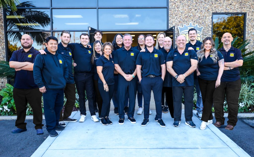 A team of 15 people, known as the Hail Squad, stands in front of a building, dressed in similar uniforms and smiling proudly.