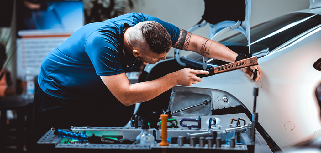 A veteran precision expert uses a specialized tool to repair a car dent, carefully working through each detail. Nearby, the organized tray holds an array of instruments, embodying the meticulous approach of The Hail Squad in hail damage repair.