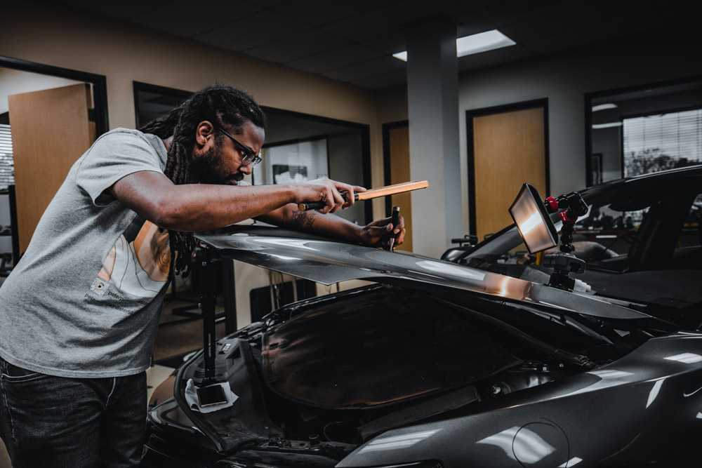 A man expertly uses a tool for Paintless Dent Repair on a car hood in the workshop.